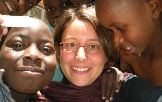 Eine Frau lächelt mit zwei afrikanischen Kindern in die Kamera 
