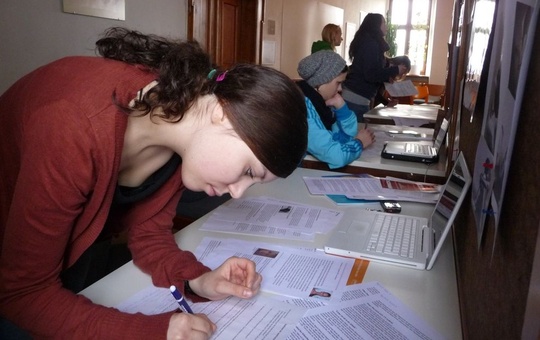 Eine junge Frau beugt sich über ein Blatt Papier und schreibt. 