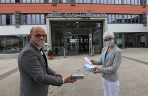 Schulreferent Jürgen Engel übergibt eine der gespendeten transparenten Coronamasken an Oberstudienrätin Anette Gerhard, die sich in der Schulpastoral am Kitzinger Armin-Knab-Gymnasium engagiert.