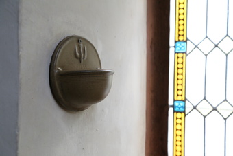 Weihwasserbecken neben Glasfenster