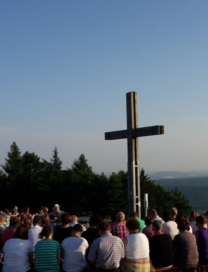 Gläubige feiern Gottesdienst neben einem Gipfelkreuz.