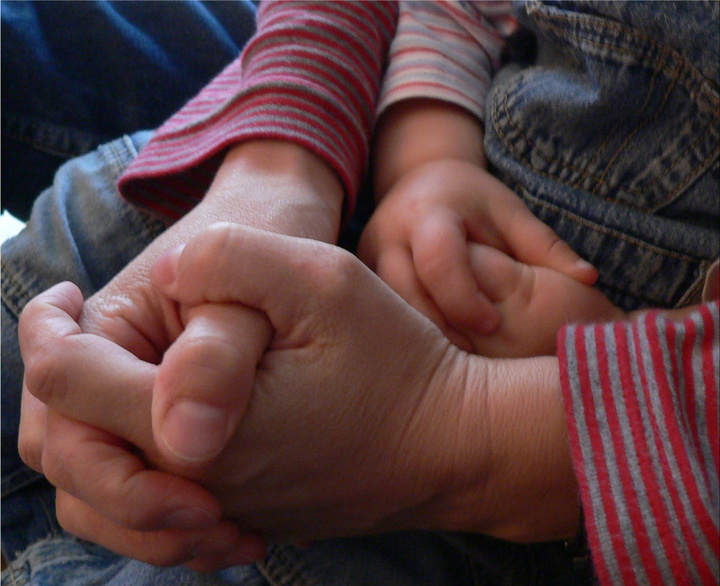 Ein Erwachsener und ein Kind beten gemeinsam. Man sieht die gefalteten Hände.