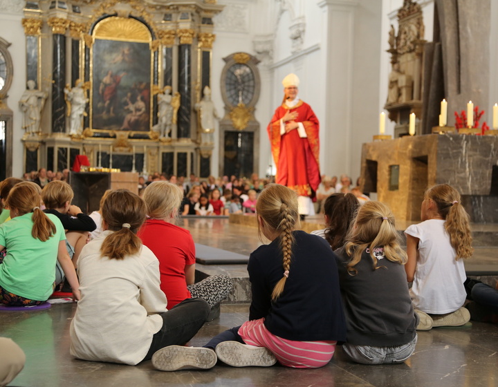Kinder sitzen mit dem Rücken zur Kamera im Chorraum des Doms und schauen zu Bischof Franz