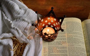Eine aufgeschlagene Bibel im Licht einer Kerze und nebenan eine Windel mit Stroh