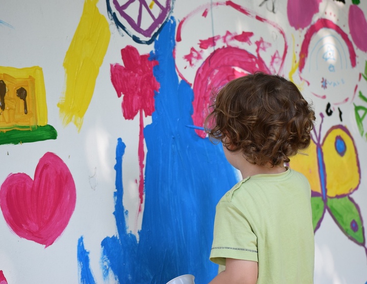 Kind malt mit Pinsel und Farbe an eine Wand. 