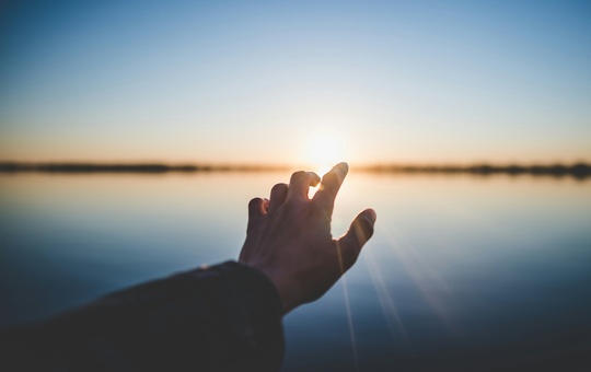 Eine ausgestreckte Hand einer Person vor der Sonne