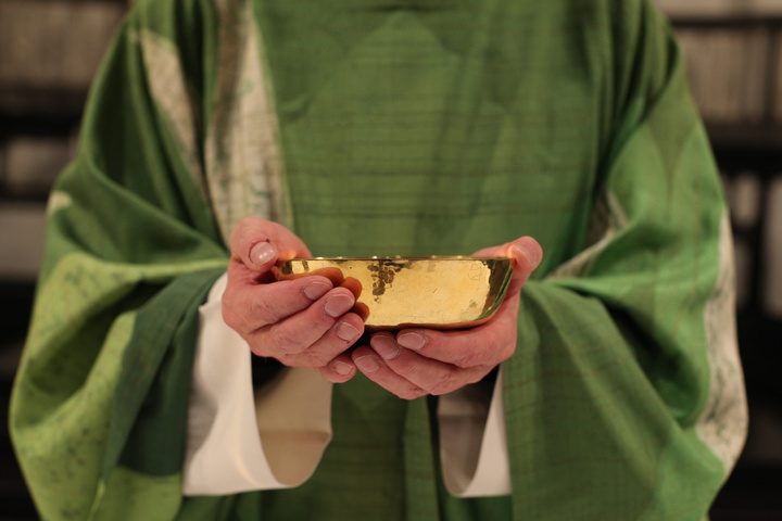 Ein Priester hält eine Patene in der Hand.