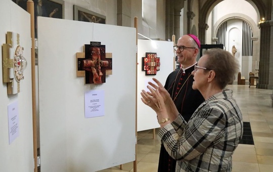 Bischof Franz und die Künstlerin Monika Baumann schauen auf eine Stellwand, an der ein Kreuz hängt