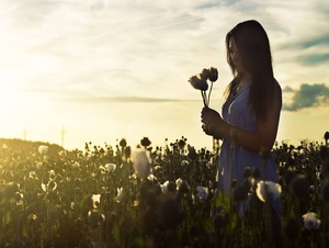 Eine Frau steht in der Abendsonne inmitten der Pflanzen eines Feldes und hält Blumen in den Händen.