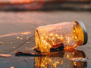 Ein Glas mit Lichterkette liegt auf einem Strand während dem Sonnenuntergang.