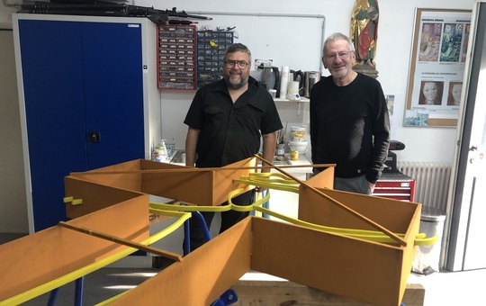 Zwei Männer stehen hinter einem großen Kreuz, das auf einem Gestell liegt