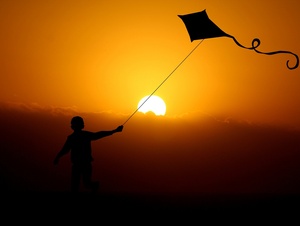 Ein Kind rennt mit einem fliegenden Drachen in den Sonnenuntergang